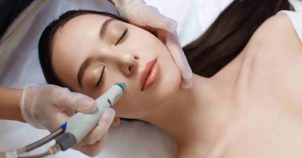 A person with long brown hair is receiving a HydraFacial® Treatment in Charleston, SC with a handheld device in a spa or clinic setting.